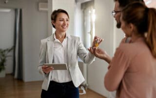 Young Happy Real Estate Agent Giving House Keys Couple Who Is Buying New Home