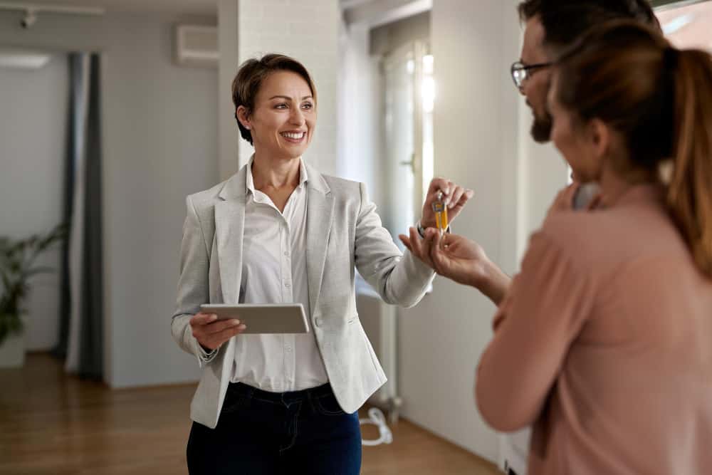 Young Happy Real Estate Agent Giving House Keys Couple Who Is Buying New Home